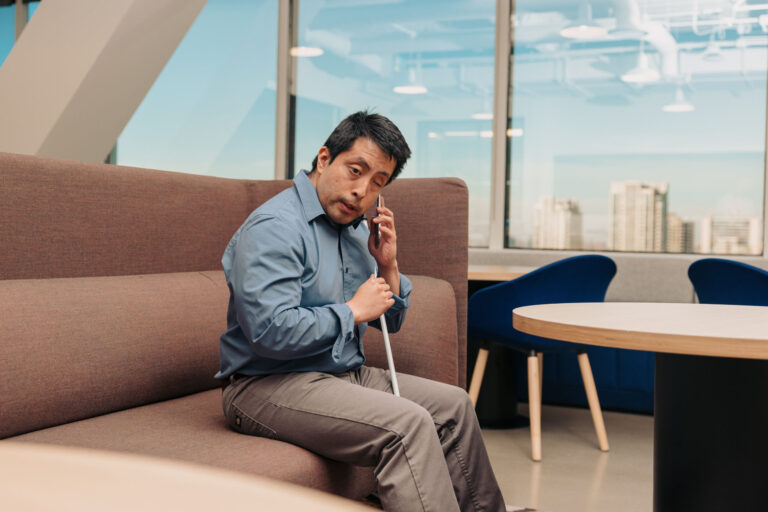 a man who is blind sits with can between his legs listening to his phone