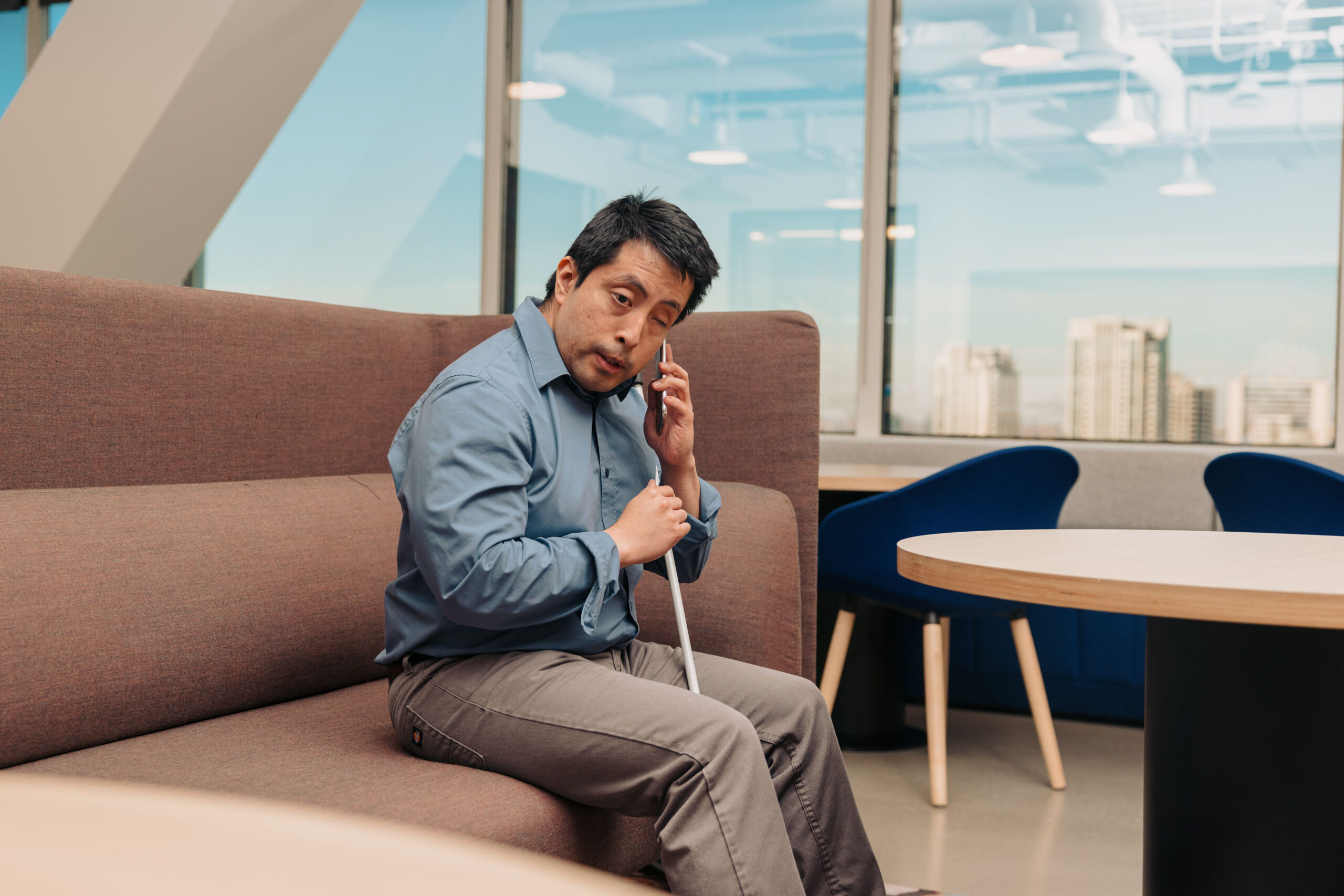 a man who is blind sits with can between his legs listening to his phone